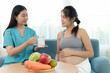 © Stella - Beautiful female nutritionist holds milk glass while consulting about essential healthy foods to happy pregnant mother. Asian pregnancy woman listens to advice from medical nurse on improving diet.