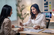 © Apichat - Two women are talking in a room with a desk in the background