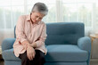 © Stella - Asian senior massaging hand suffering from wrist pain while sitting on sofa at living room. Unwell mature rubbing hand, feeling hurt joint pain at home. Unhappy elderly grandma suffers from wrist pain