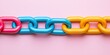 © Anucha - A vibrant, colorful chain made of interlinked plastic links on a pink background, showcasing a playful and modern design.