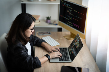 Wall Mural - a woman is typing on a laptop computer in front of two monitors. she is wearing glasses and is focus