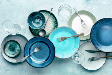 Modern tableware, overhead flat shot. A table setting with plates, forks, and glasses, shot from the top on a slate background