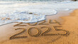 © Lahiru - 2024 to 2025 written text on beach sand & sea wave background. coming happy new year celebration concept.