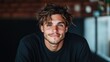 ©  Shomixer - A young man casually relaxed indoors wearing a black shirt, with a laid-back demeanor captured in a softly blurred background, radiating calm and modern fashion.