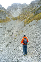 Wall Mural - A tourist with a backpack, photographed from behind, looks at the scree below the summit while standing on a hiking trail in the Ljubokuć valley, also known as Lugo i kuq (Prokletije National Park)