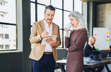 Fototapete - Two professionals engage in a discussion at a stylish office, with one taking notes while the other enjoys a warm beverage, highlighting collaboration and idea exchange in a contemporary setting.