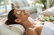 © SerPak - A woman enjoys a tranquil spa treatment, reclining with cucumber slices placed on her eyes. Surrounded by a peaceful indoor setting, she experiences relaxation and rejuvenation, highlighting self care
