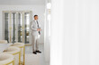 © Vasil - A man in a suit stands in front of a window, looking out. The room is decorated with white furniture and has a modern, minimalist style