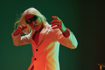 Wall Mural - Stylish man in a sleek white suit posing dramatically with long white hair and sunglasses against a vibrant green background The image has an energetic and stylish vibe, showcasing contemporary