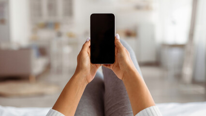 Point of view of black woman holding cellphone with blank empty screen for mock up in hands, young lady browsing social media or using app, lying on couch at home, selective focus, blurred background