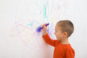 happy smiling baby boy holding marker and drawing colorful scratches lines on white wallpaper backgr