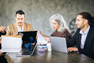 Leinwandbilder - A diverse group of professionals engage in a brainstorming session around a table, using laptops and discussing ideas in a contemporary office environment.
