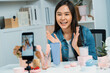 © Summit Art Creations - Young beautiful Asian girl reviewing cosmetic and skin care product with new collection's promotion selling on social media online live blurred phone screen surrounded beauty merchandise. Stratagem.