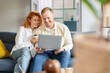 © Home-stock - Young European couple drinking coffee and looking at laptop screen, shopping online or searching movie while sitting on sofa at home