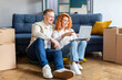© Home-stock - Happy spouses buying decor via laptop, sitting among carton boxes in new apartment, couple having video call and telling about relocation to family