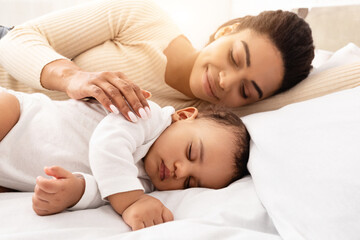 Wall Mural - Loving Black Mom Hugging Sleeping Baby Lying In Bed In Bedroom At Home. Toddler Infant Sleeps Near Mom. Motherhood Lifestyle, Daytime Sleep Routine Concept. Selective Focus