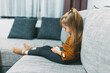 © Milos - Seated comfortably on a plush sofa, a child immerses herself in digital exploration on a smartphone, illustrating a slice of modern domestic life.