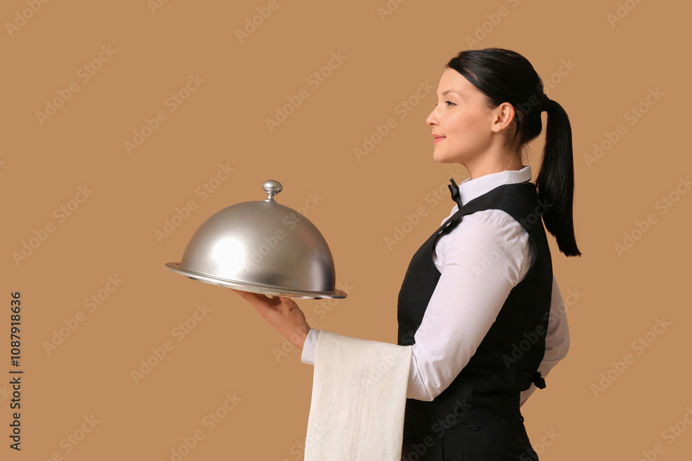 Beautiful young waitress with tray and cloche on brown background