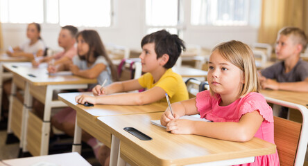 Wall Mural - Young schoolgirls and schoolboys studying in classroom during their lesson.