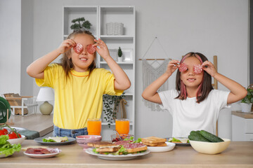 Wall Mural - Funny little girls with sausages making toasts in kitchen