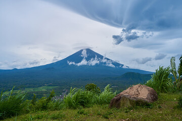 Wall Mural - A viewpoint with a large stone and a view of the sacred volcano Agung covered with clouds on a rainy day on the island of Bali. View of the mountain.