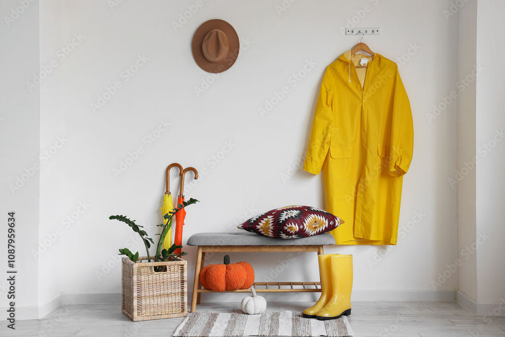 Interior of light hallway with yellow raincoat, umbrellas and soft bench