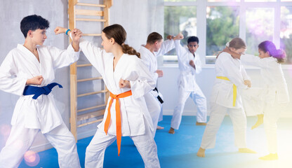 Wall Mural - Boy and girl in kimono practicing karate techniques in group in studio..