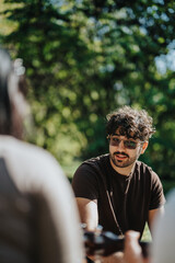 Poster - A young man with sunglasses enjoys a sunny day outdoors, engaged with friends in a park setting, surrounded by lush greenery.