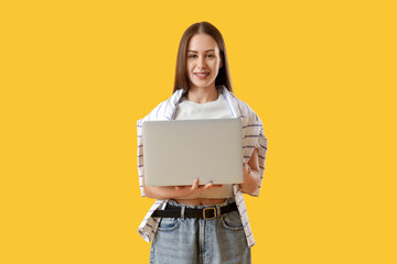 Young woman using modern laptop on yellow background