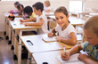 © JackF - Focused girl sitting at desk writing test in classroom full of pupils during lesson