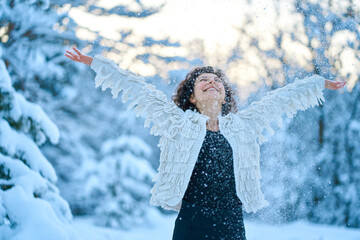 Wall Mural - A woman happily playing with snow in a snow-covered winter forest