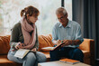 © qunica.com - A senior professor assists a female student with her notes. They engage in a thoughtful discussion in a comfortable setting, showcasing mentorship and learning.