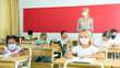 © JackF - Primary school students in protective masks sit at school desk in the classroom