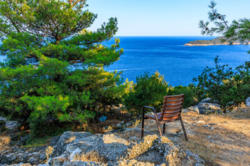 Wall Mural - A wooden chair is sitting on a rocky hill overlooking a body of water