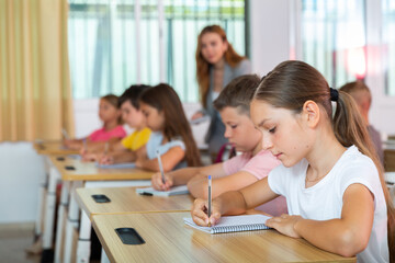 Wall Mural - Pupils sitting in classroom during lesson. Female teacher standing behind.