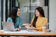 © Satori Studio - Two Young Women Collaborating in a Modern Office Setting with Laptops and Documents