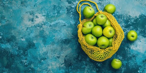 Poster - A yellow string bag filled with green apples rests on blue concrete. The image includes copy space and is viewed from above.