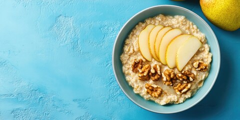 Aufkleber - Healthy breakfast: A bowl of porridge topped with pear slices and walnuts on a blue background. Flat lay. Copy space. Top view.