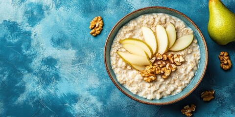 Aufkleber - Healthy breakfast: A bowl of porridge topped with pear slices and walnuts on a blue background. Flat lay. Copy space. Top view.