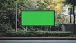 © Phatharaporn - A blank green billboard stands in a park-like setting, surrounded by greenery and trees, ready for advertising or creative displays.