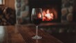 © Cyber Shutter - Red wine glass on a wooden table with a cozy fireplace glowing warmly in the background, creating an inviting atmosphere.