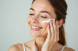 © Alena - Positive young female in white top with closed eyes applying moisturizing cream on face