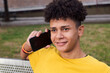 © Raul Mellado - smiling latin teen male with curly hairstyle talking on mobile phone sitting in a bench of a park, concept of youth and technology of communication