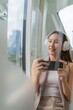 © StockPhotoRepublic - Asian Woman Using Phone and Headphones Listening To Music and Playing Games While Commuting To Work in a Public Train