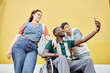 © Seventyfour - Minimal pop color shot of inclusive group of young people taking selfie photo outdoors against bright yellow wall copy space