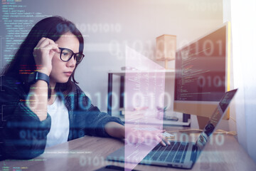 Wall Mural - coding computer programmer,a woman is sitting at a table with a laptop and computer monitor. she wor