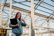 © standret - Holding notepad. Young redhead woman is standing near unfinished building, construction