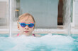 © danr13 - Caucasian girl wearing colorful swimming goggles standing in a pool under a cascading water stream