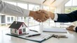 © Liana - Two people shaking hands over a desk with house model and keys, symbolizing a real estate deal, contract signing, or successful negotiation. Bright office setting emphasizes professionalism.