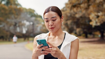 Happy, fitness and Japanese woman with cellphone in park searching for online exercise program for health. Sports, phone and female athlete typing on browsing website for workout routine outdoor.